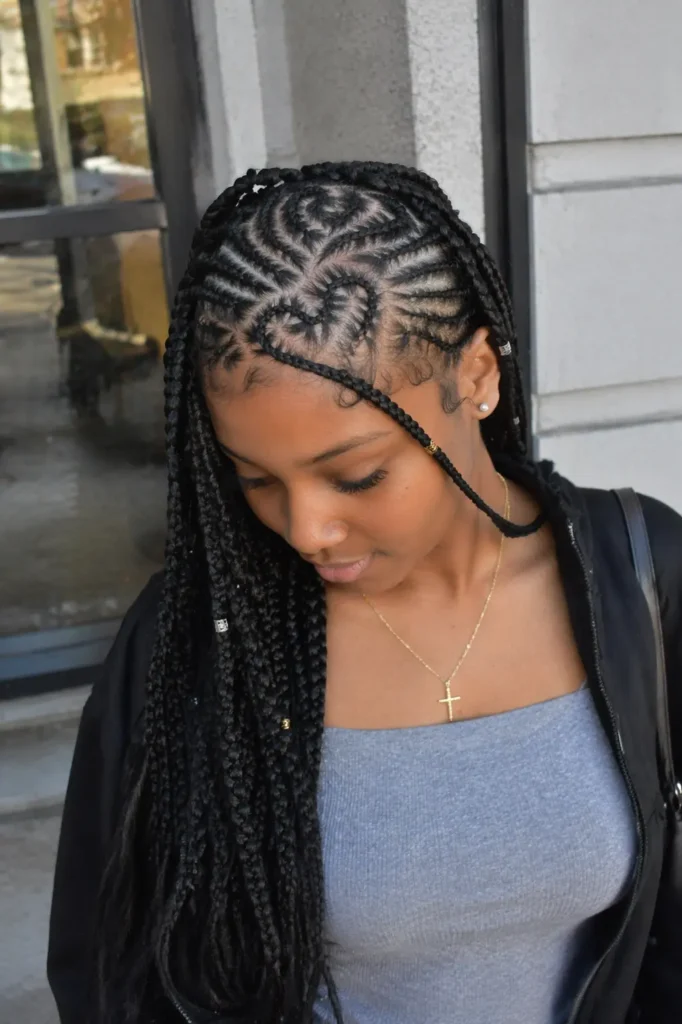 young woman with Fulani braids styled into intricate heart-shaped cornrow patterns on her scalp, with long braids cascading over one shoulder