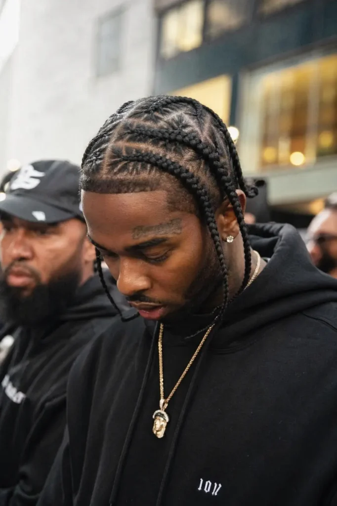 a Black man with Pop Smoke–inspired braided hairstyle, featuring clean, symmetrical cornrows with defined parts. He wears a black hoodie and gold chain,