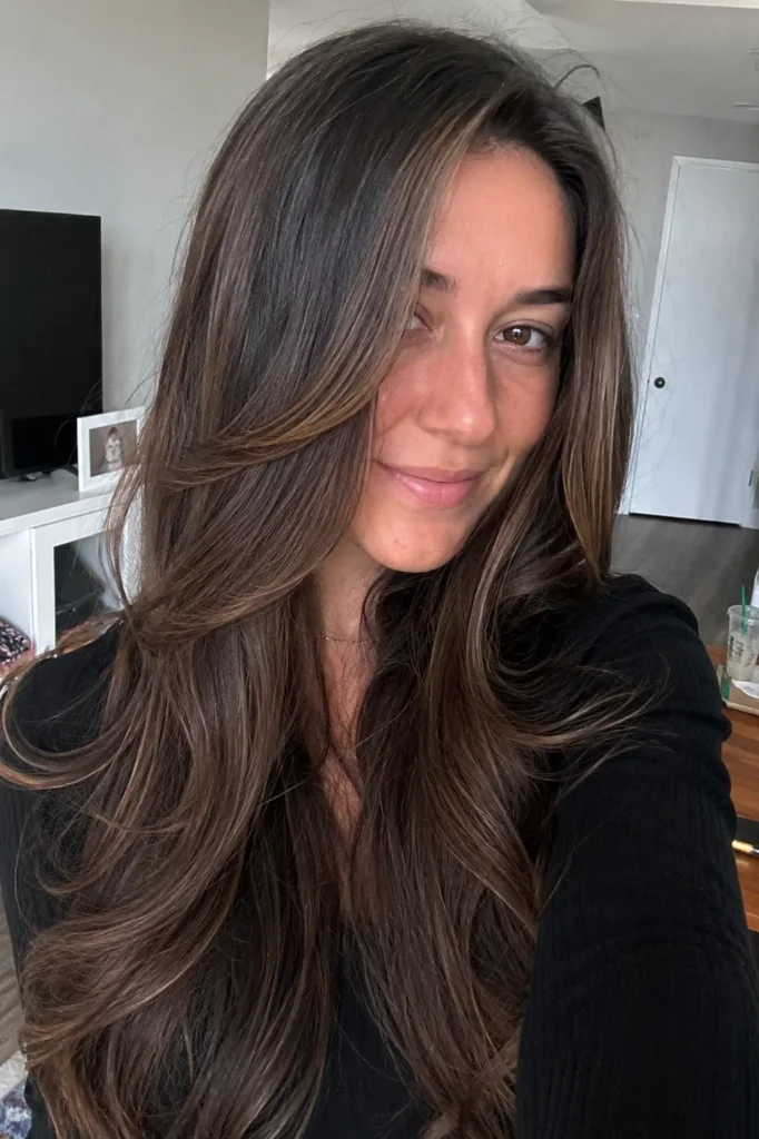 A realistic vertical portrait of a young woman with long dark brunette hair featuring subtle ash mocha babylights, styled in soft layers