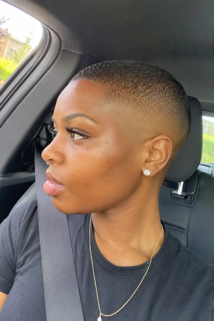 a Black woman in her late 20s to early 30s with a clean bald fade buzz cut, natural facial features, and authentic skin texture. She has a calm everyday expression while the hairstyle remains the focal point,