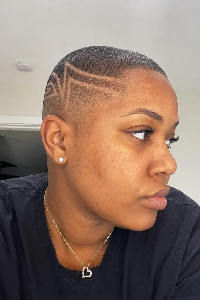 f a Black woman around 25–35 years old with a bald fade hairstyle featuring detailed shaved line designs.