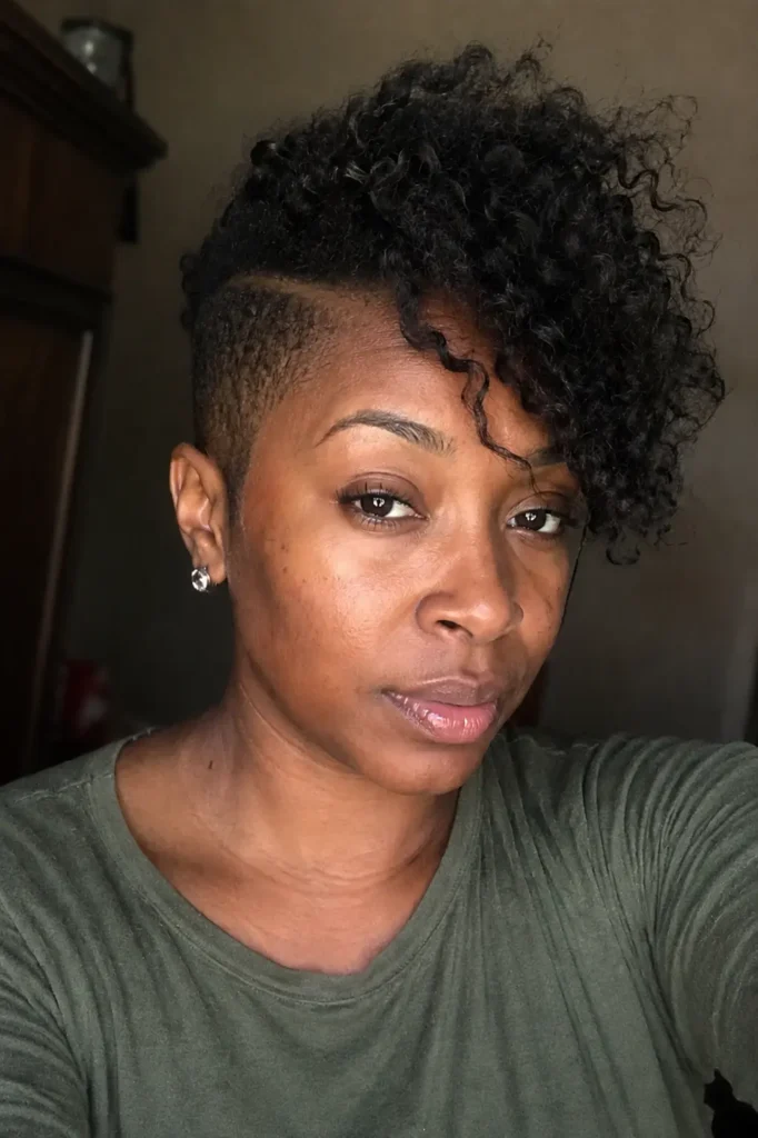 a Black woman in her late 20s to early 30s with a side-swept textured bald fade hairstyle featuring defined curls and natural movement