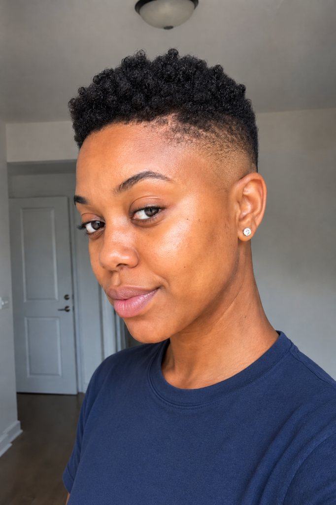 a real Black woman with a bald fade hairstyle and tight coil texture on top, wearing a modest navy blue crew-neck shirt.
