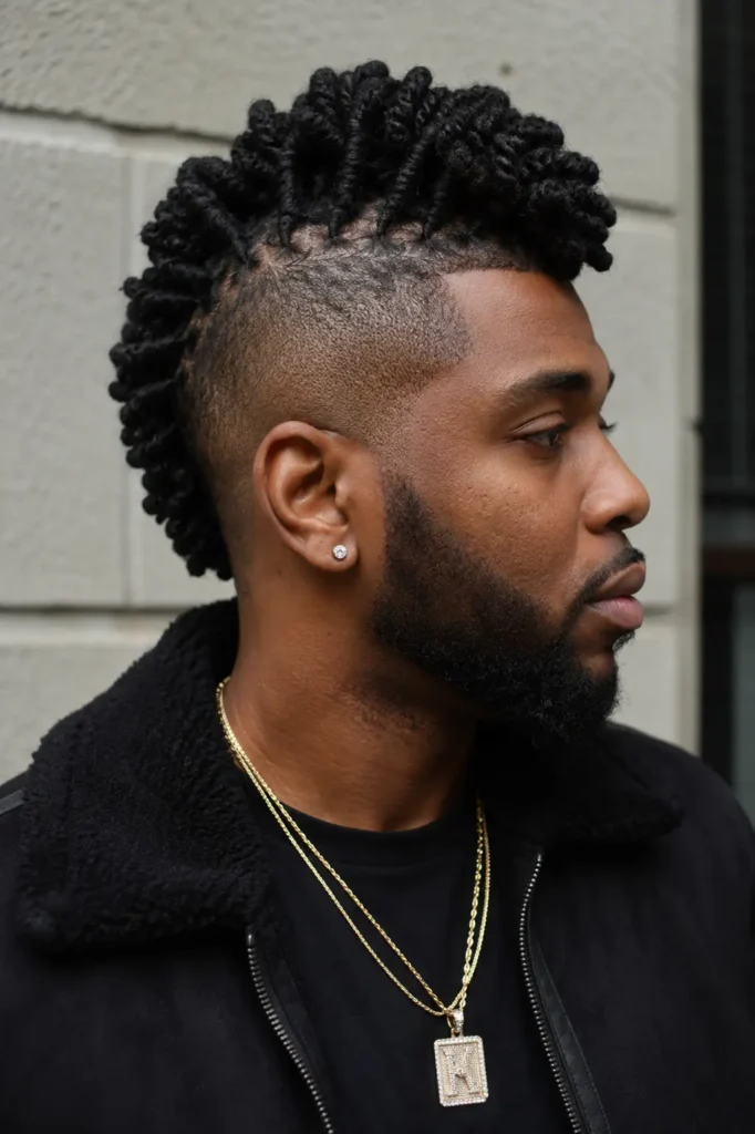 an African American man with a barrel twist loc mohawk hairstyle and shaved sides, shown in side profile. He has natural skin texture, authentic facial features, and a neatly groomed beard. Wearing a dark urban-style jacket and layered gold chains,
