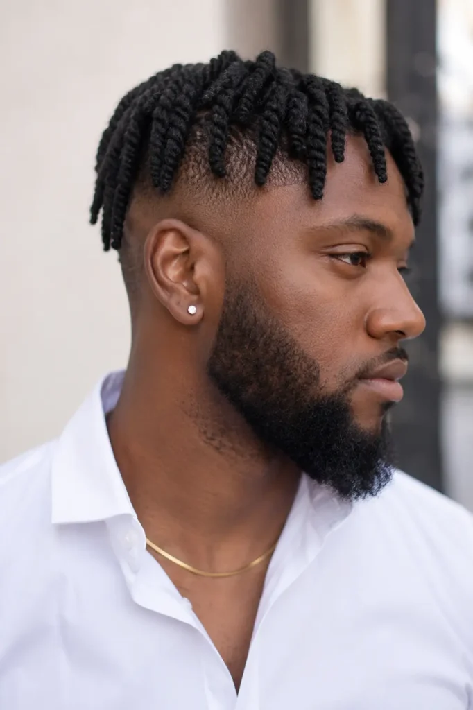 Black man with barrel twist locs styled over an undercut haircut, shown in a realistic vertical portrait. He wears a crisp white shirt and a neatly groomed full beard.