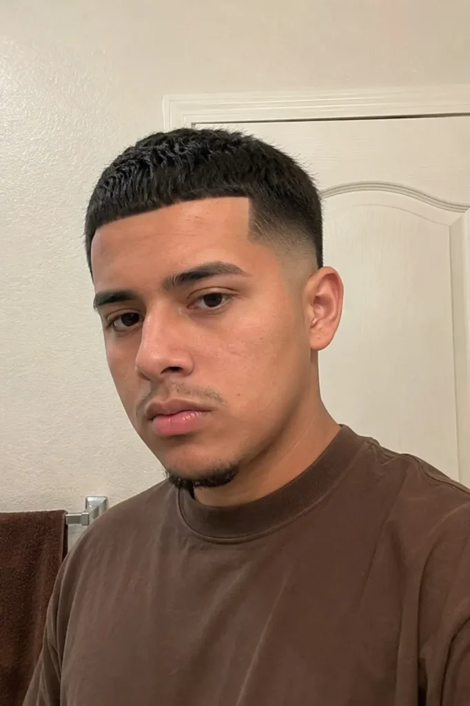 a young man in a brown shirt with a Caesar cut fade and sharp edge up haircut, featuring clean fringe details