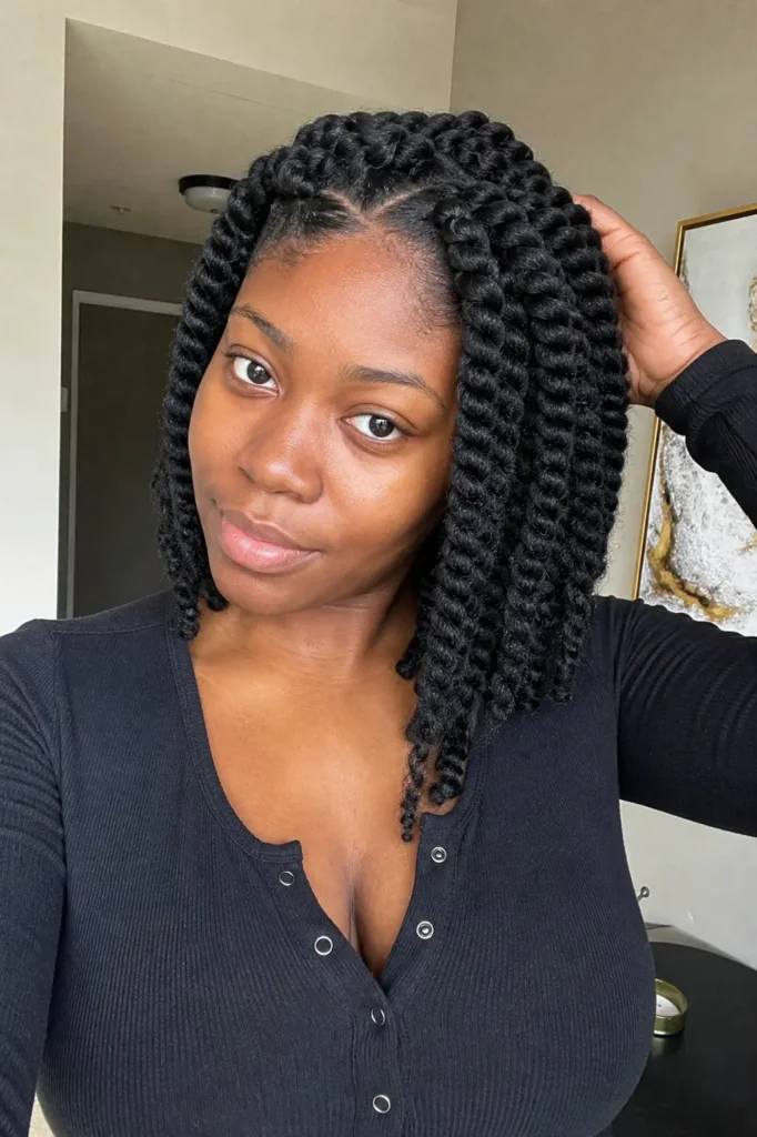 a young Black woman with chunky two-strand twists parted down the middle. She gently holds one side of her thick twists,