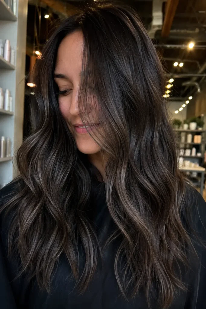 girl with dark hair featuring cool smoky ash babylights styled in loose waves, captured in a candid portrait with soft natural lighting