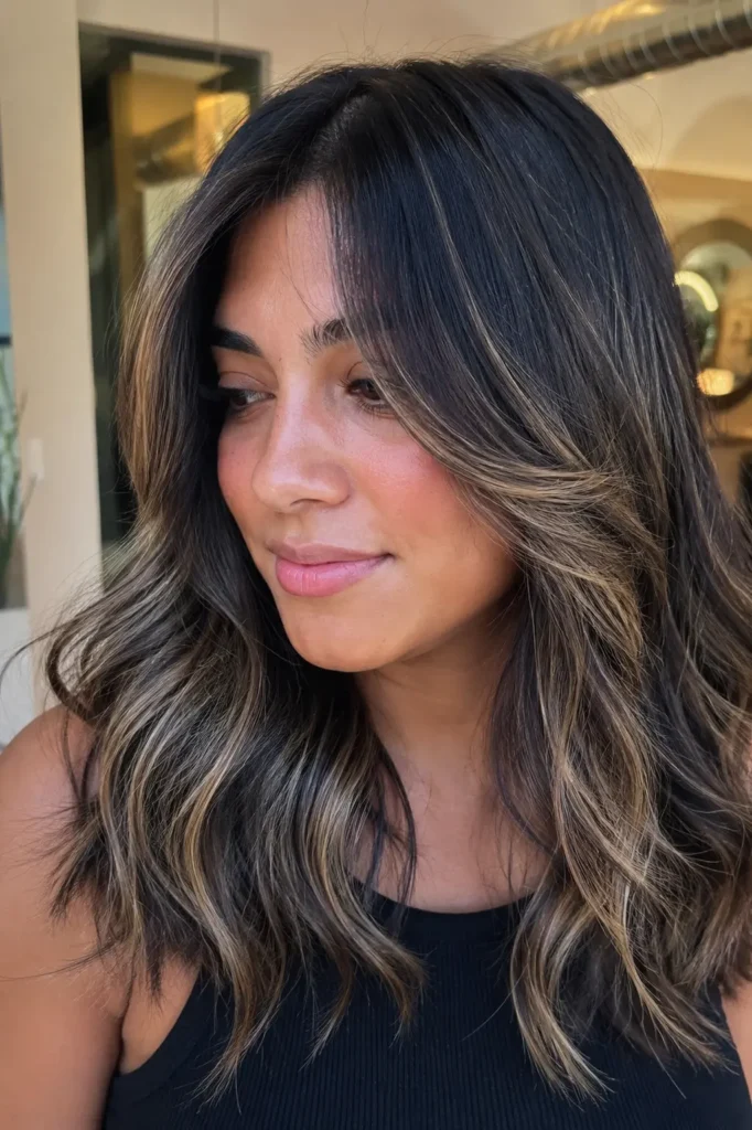 a young woman with dark hair and face-framing ash blonde babylights, styled in soft layered waves