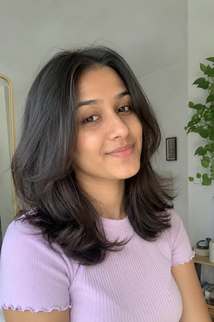 young woman with medium-length dark brown hair styled with smooth roots and softly flipped ends, wearing a pastel lavender top