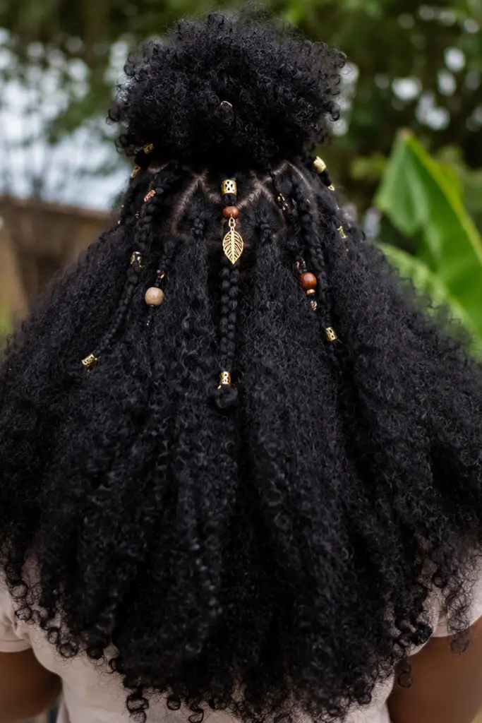 Back view of a real Black woman outdoors wearing a half-up half-down afro hairstyle with voluminous natural curls flowing down her back.