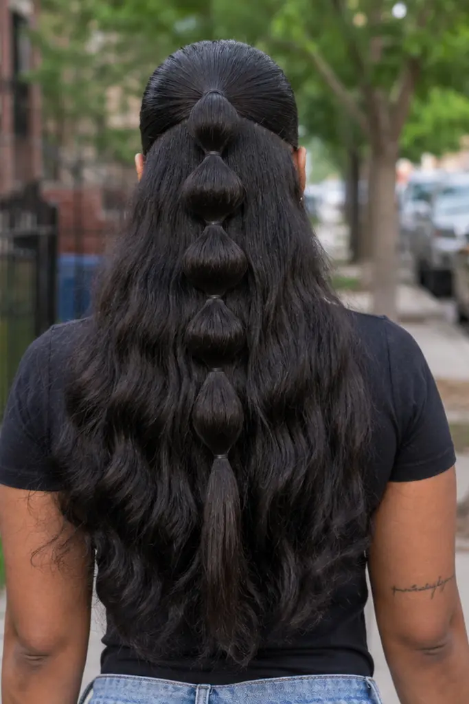 Back view of a real Black woman wearing a sleek half-up half-down bubble ponytail hairstyle with multiple rounded bubble sections cascading down the center.