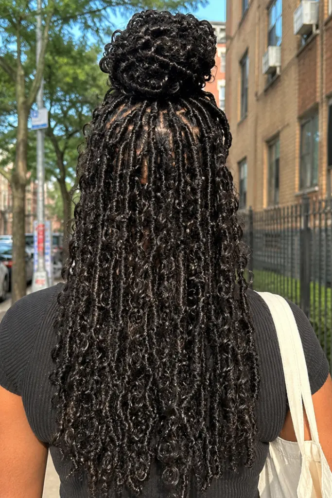 Back view of a real Black woman wearing a butterfly locs half up half down hairstyle with textured, messy locs cascading down her back