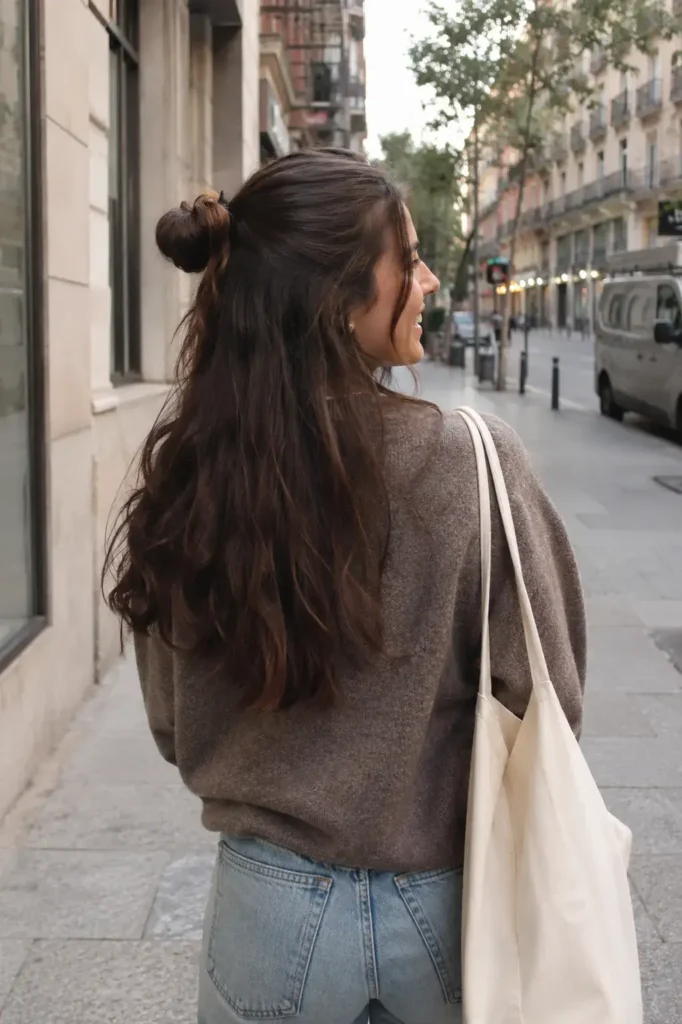 A real girl with a half-up half-down hairstyle viewed from the back on a city street, wearing a cozy casual outfit with soft natural lighting and medium wavy hair texture.