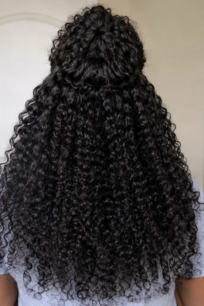 Back view of a real Black woman wearing a curly half up half down wig hairstyle with voluminous natural curls cascading down her back.