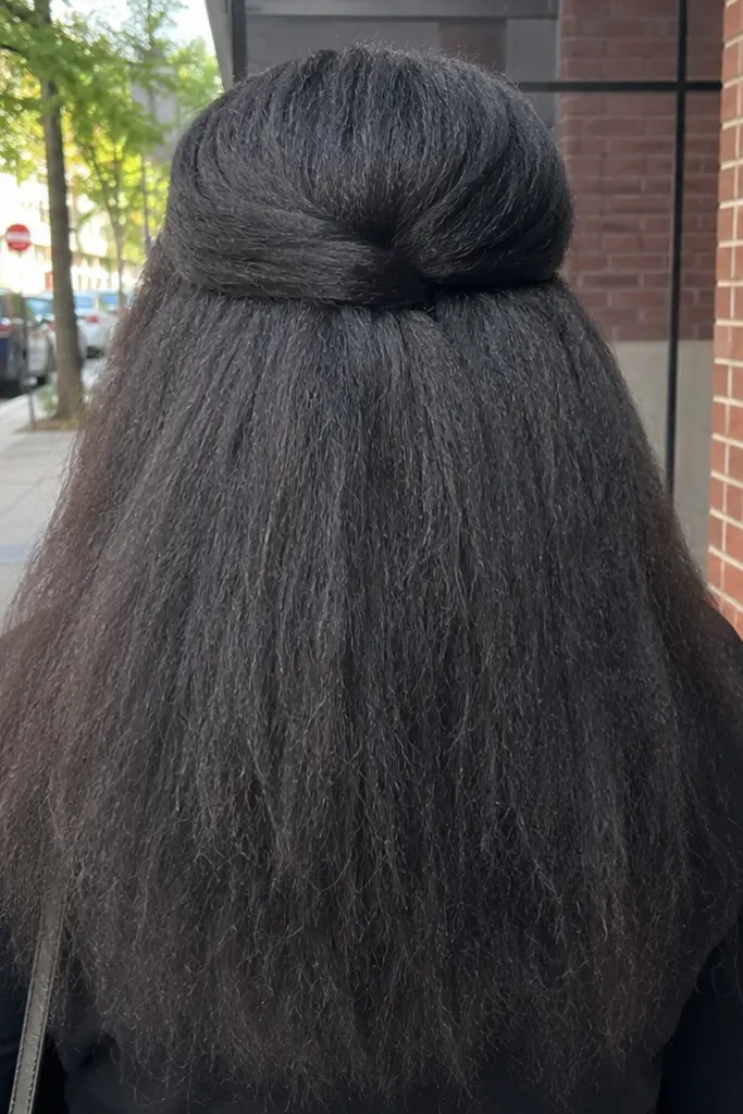 Back view of a real Black woman wearing a kinky straight half up half down hairstyle with blown-out textured hair flowing naturally down her back