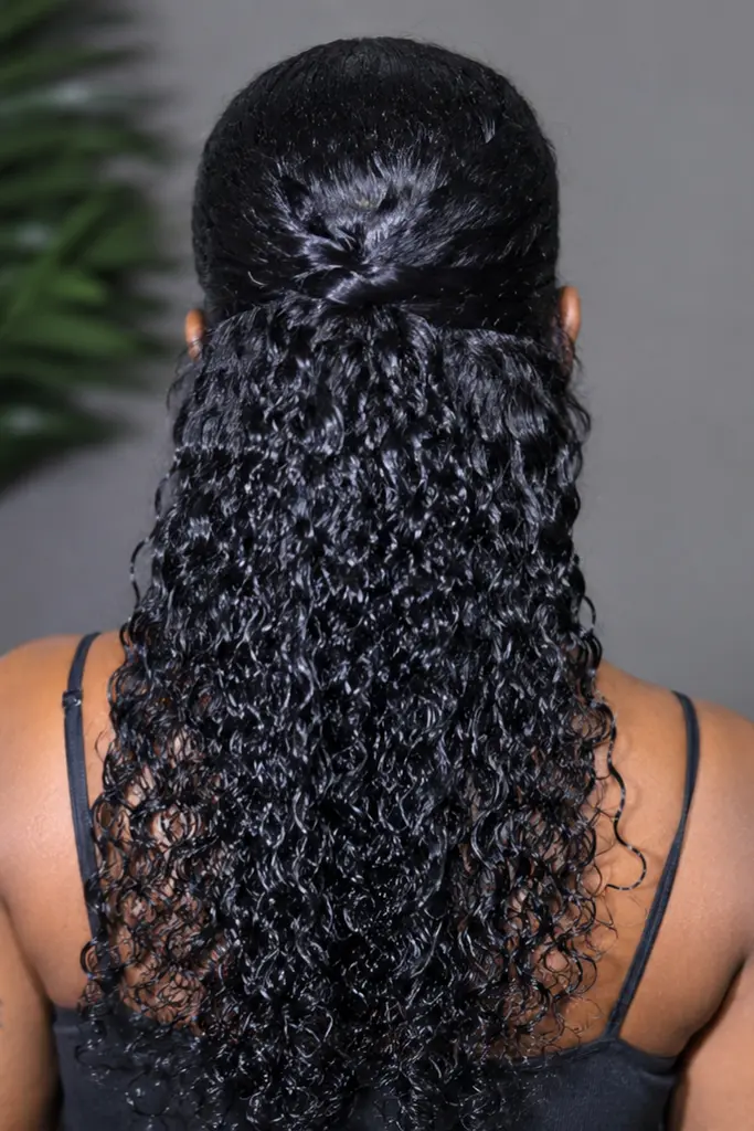 Back view of a real Black woman wearing a half-up half-down wet look curls hairstyle, with glossy defined curls cascading down her back