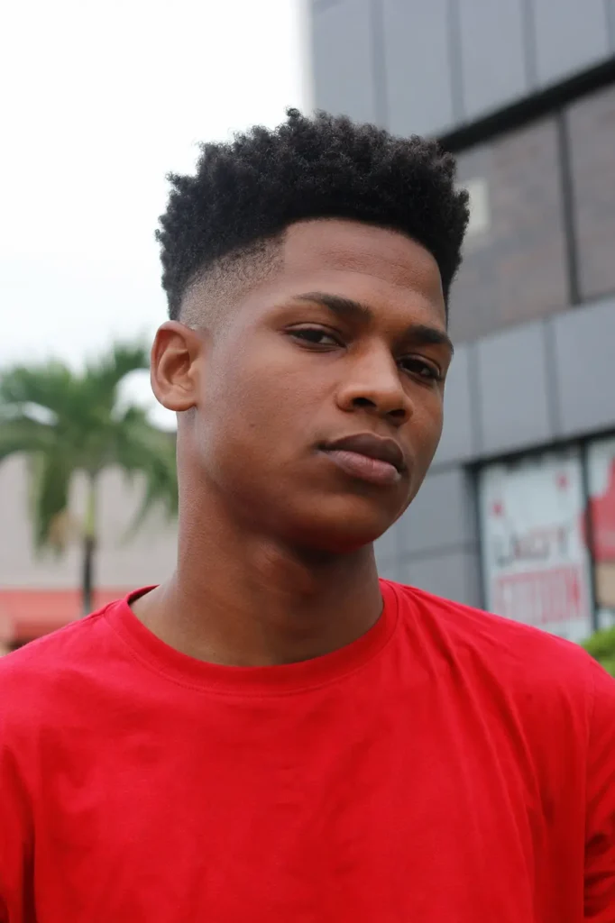 a young man in a red shirt with a high top fade haircut and textured styling, featuring authentic skin texture,