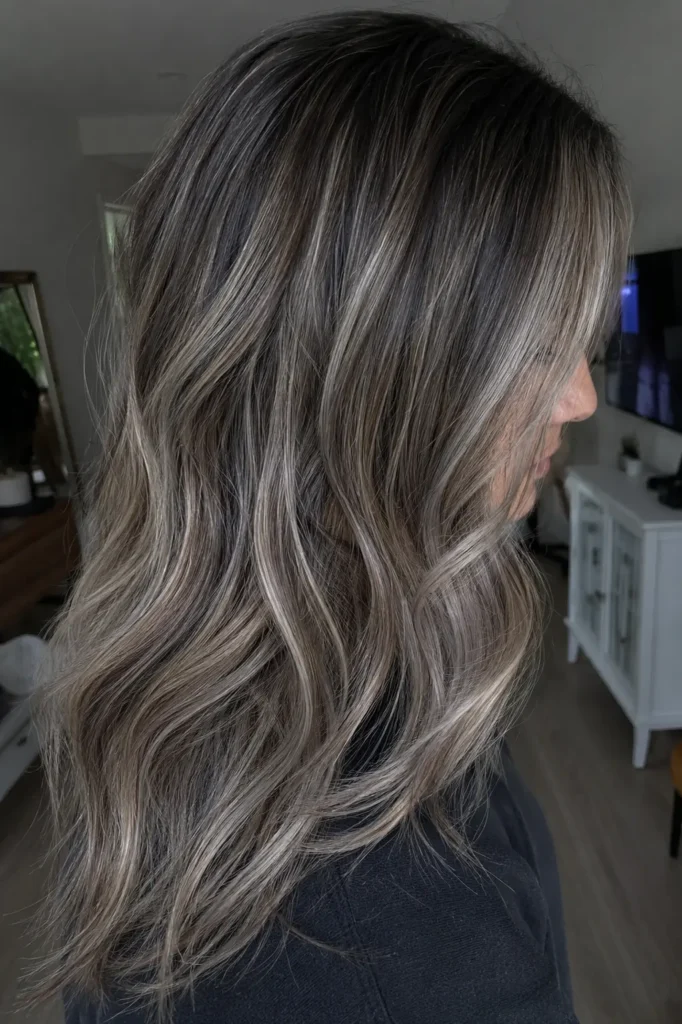 Soft layered waves with a dark root melt blending into icy ash babylights, photographed in realistic home lighting