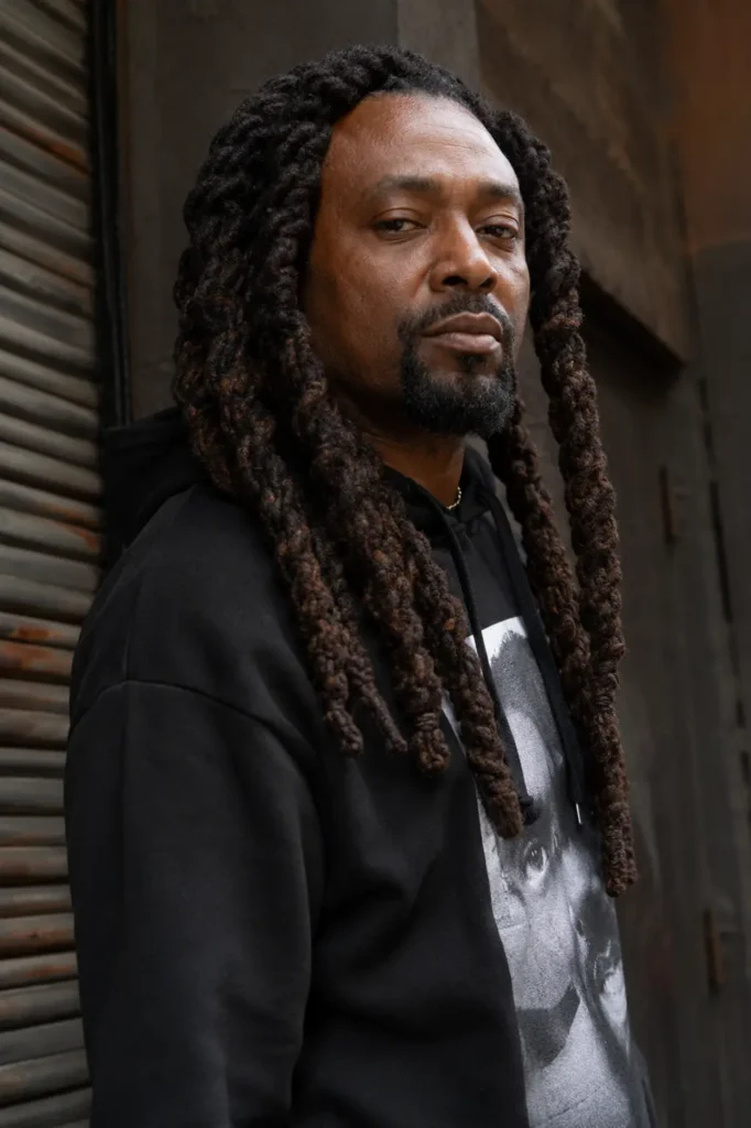 a mature Black man with jumbo barrel twist locs styled into thick, defined twists that frame his face and fall past his shoulders. He has authentic skin texture, a neatly groomed goatee, and a confident expression