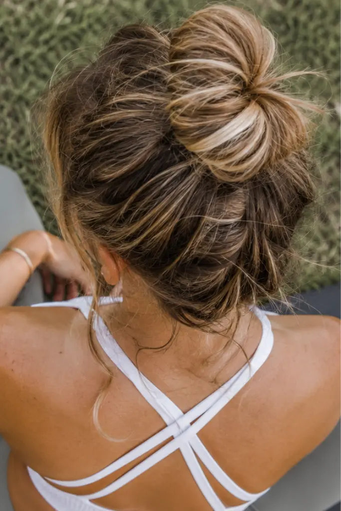 Messy top knot bun hairstyle on a real college girl with light brown wavy hair, photographed from an overhead back view in an outdoor park