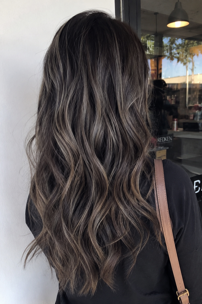 a woman with long dark brunette hair featuring shadow root ash babylights and soft loose waves