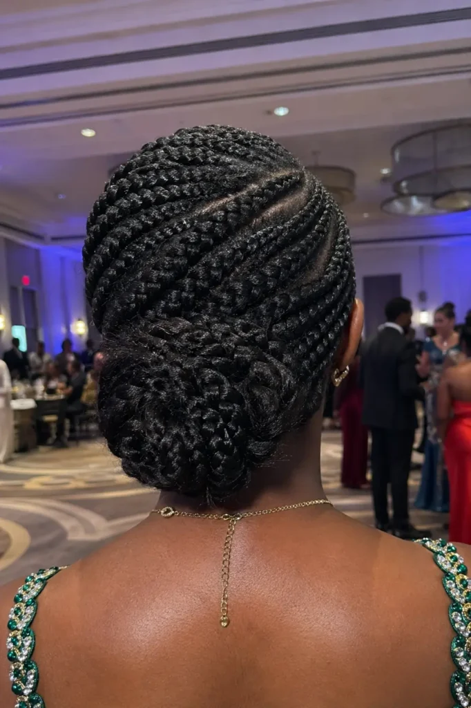 Back view close-up of a Black teenage girl’s head at prom, featuring a side-swept braided style gathered into a low bun at the nape