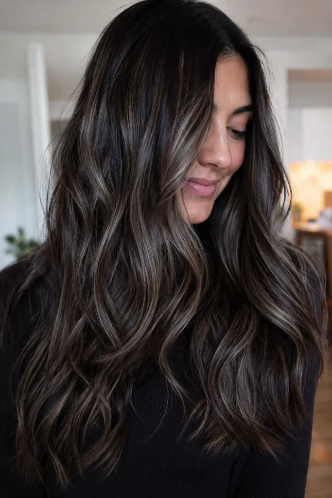 a brunette woman with long layered hair and soft waves, featuring dimensional silver ash babylights woven throughout dark brown tones