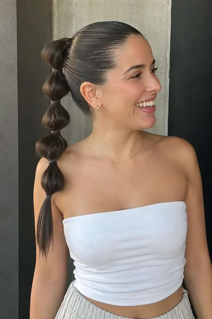 Smiling young woman with a sleek front bubble ponytail hairstyle featuring glossy bubble sections, natural makeup,