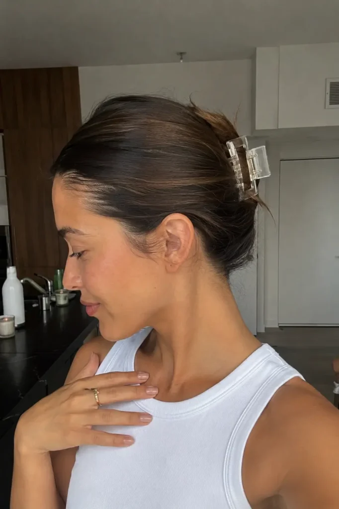 a young woman with a slicked front claw clip hairstyle, featuring glossy sleek roots, soft clip-up volume,