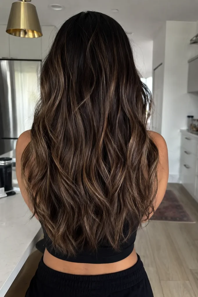 a real woman with long dark hair featuring soft ash caramel babylights and textured loose waves,