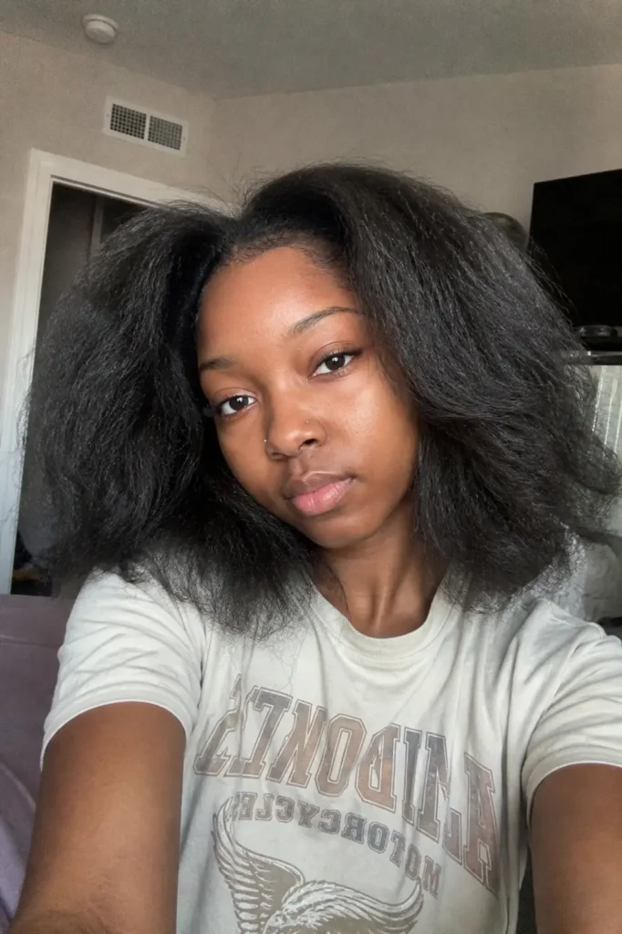 a selfie of a young Black woman with a stretched blowout afro, showing full, voluminous natural hair , wearing a casual light-colored T-shirt.