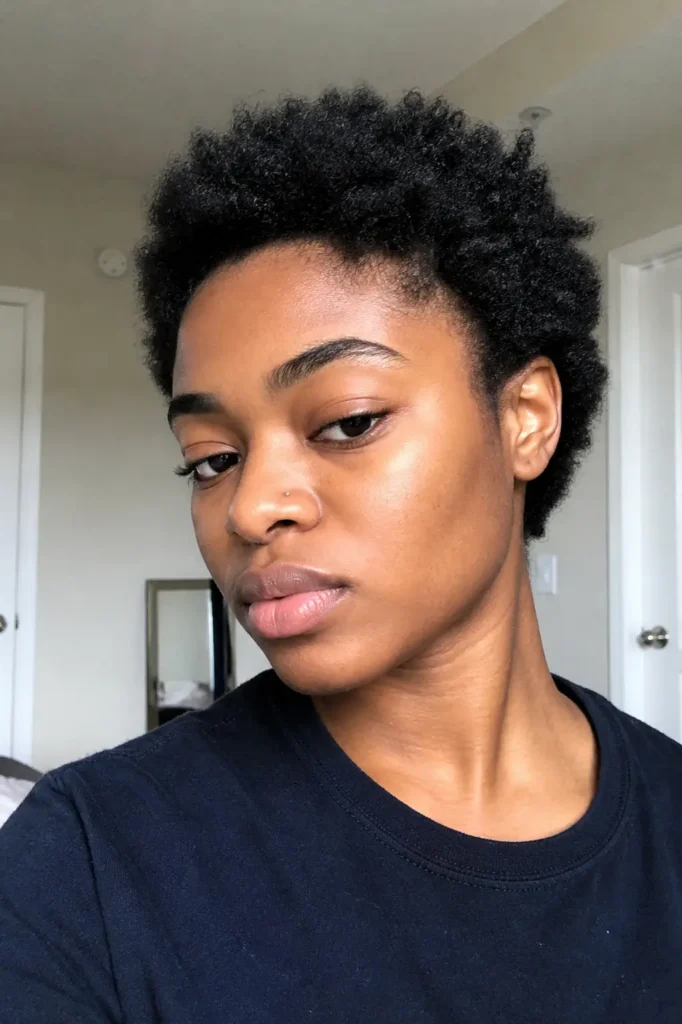 Close-up portrait of a young Black woman with a short teeny weeny afro, natural curls, and minimal makeup, captured in soft indoor daylight with realistic skin texture and a calm, candid expression.