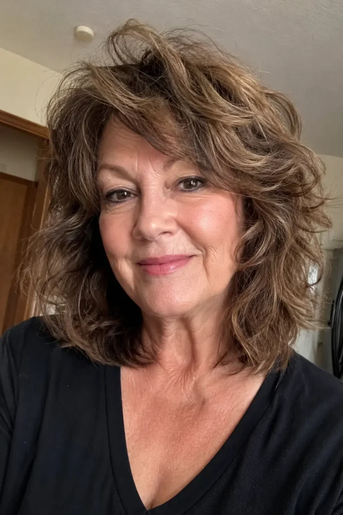 a woman around 50–60 years old with a textured collarbone-length hairstyle featuring soft layers and natural volume. Her authentic facial features and realistic skin texture are visible, with gentle movement adding fullness to the hair.