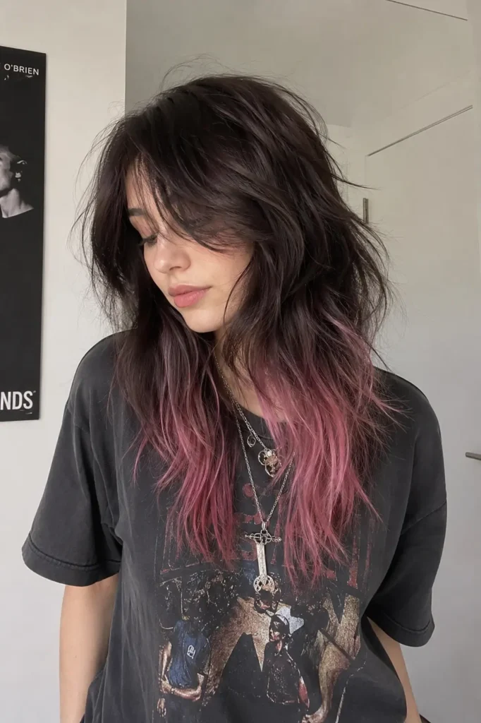 girl with a trendy wolf cut hairstyle featuring textured feathered layers and messy soft waves. The hair fades into pastel pink ends with realistic shine and movement under natural indoor light. She wears an edgy casual outfit