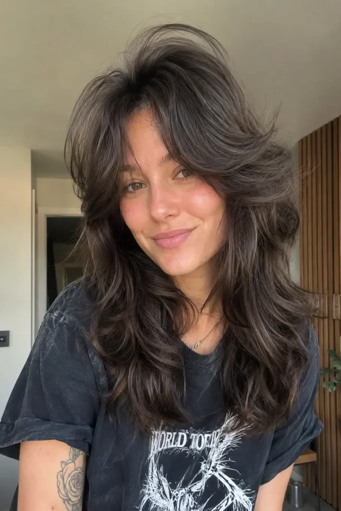 real young woman with a voluminous wolf cut hairstyle featuring dramatic crown lift, feathered textured layers, and soft curtain bangs. Her dark glossy hair has natural movement and shine under indoor daylight
