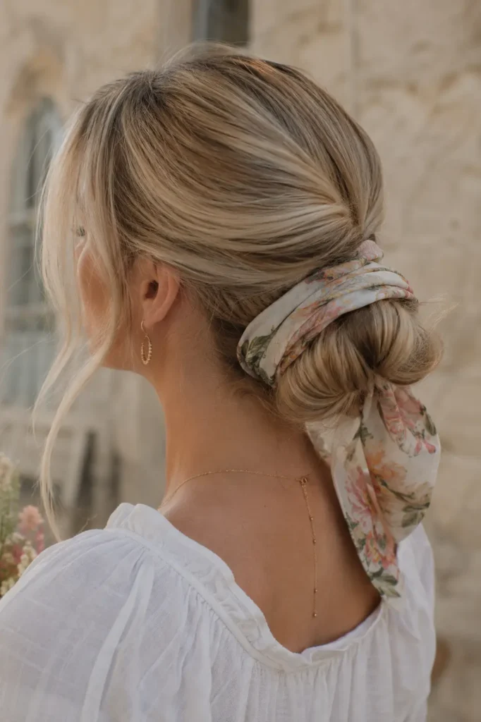  Real English woman with ash blonde hair styled in an elegant low bun wrapped with a pastel floral bandana, photographed in soft natural daylight with detailed hair texture and a relaxed outdoor setting.
