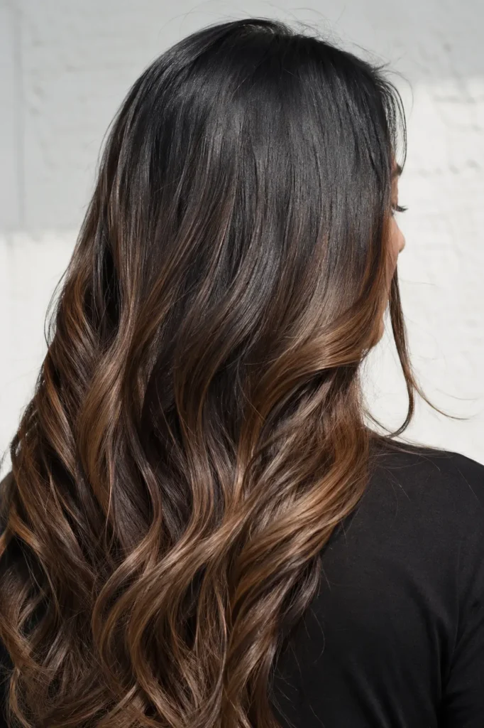oman shown mostly from the back with a slight side profile. Her long black hair blends into rich brown ombré highlights, creating a glossy, silky finish under bright natural daylight