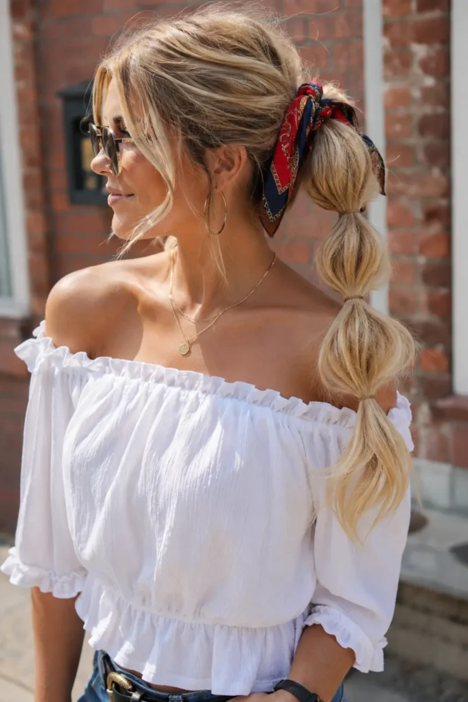 Blonde woman wearing a patterned bandana with a stylish bubble ponytail hairstyle, photographed outdoors in natural daylight.