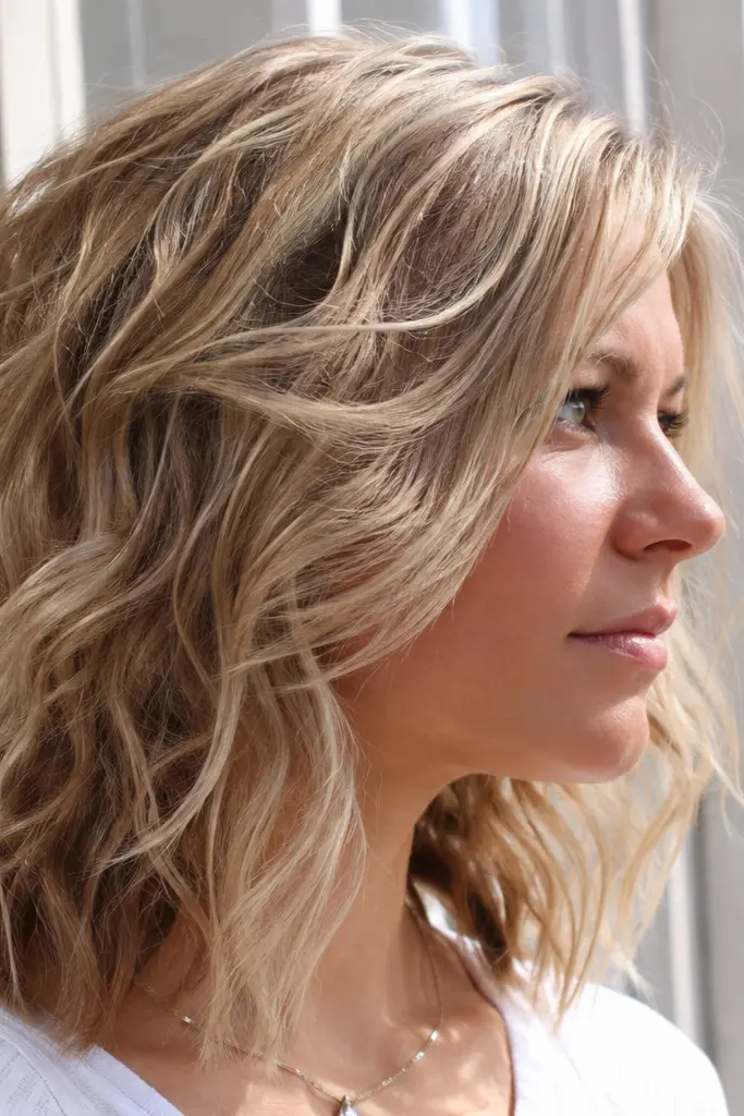 **SEO-optimized alt text:**
English woman with a choppy layered haircut and loose waves, creamy ash blonde hair, natural skin texture, and bright summer daylight portrait.
