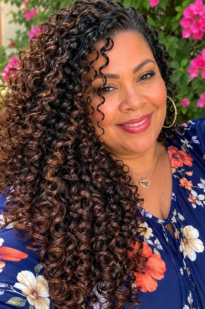 Close-up portrait of a real plus-size woman aged 30–55 with long, defined spiral curls cascading from roots to ends. Her glossy, tightly coiled curls dominate the frame, showcasing exceptional curl definition and shine. She wears a modest navy blue top