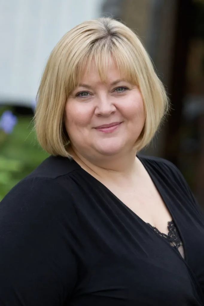 Plus-size English woman with a classic French bob haircut and soft bangs, featuring golden blonde hair with a healthy shine. Hairstyle-focused outdoor portrait captured in natural daylight