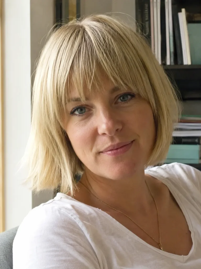 English woman with a short blunt bob haircut and soft bangs, light blonde hair framing her face, photographed in bright natural light