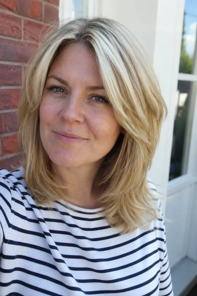 English woman with a soft wedge haircut and voluminous blonde hair in a natural daylight portrait.
