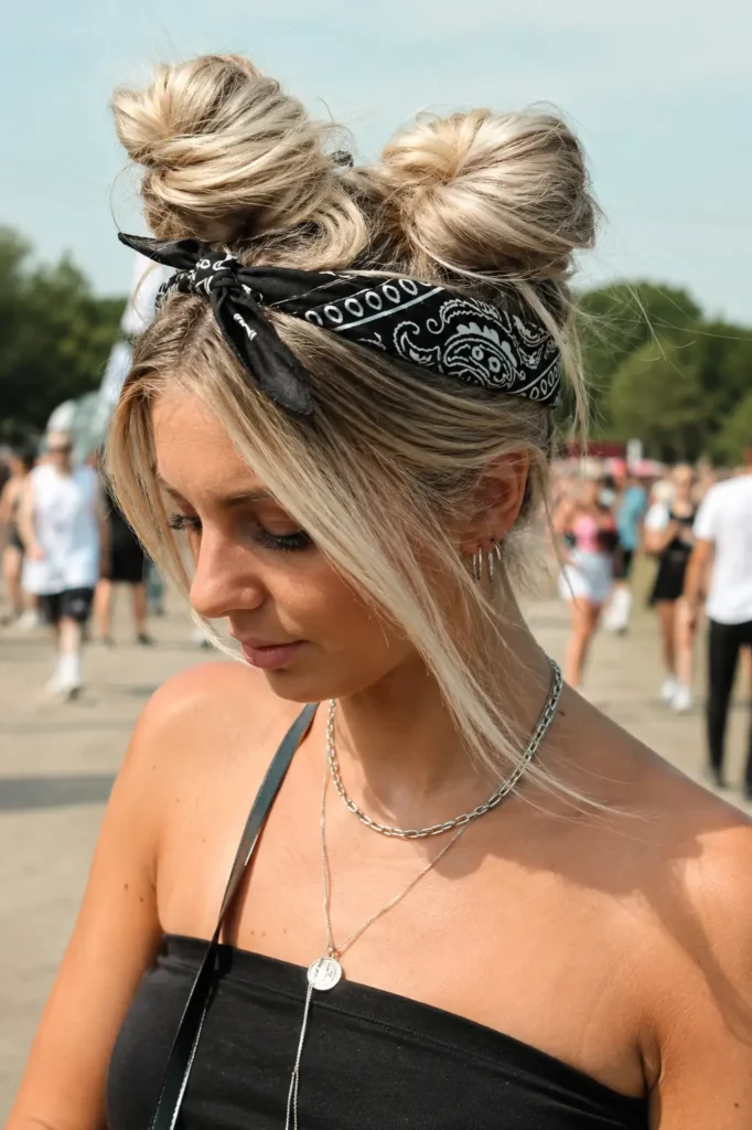 English woman with light ash blonde hair styled in space buns and a patterned bandana, photographed outdoors at a summer festival in bright daylight