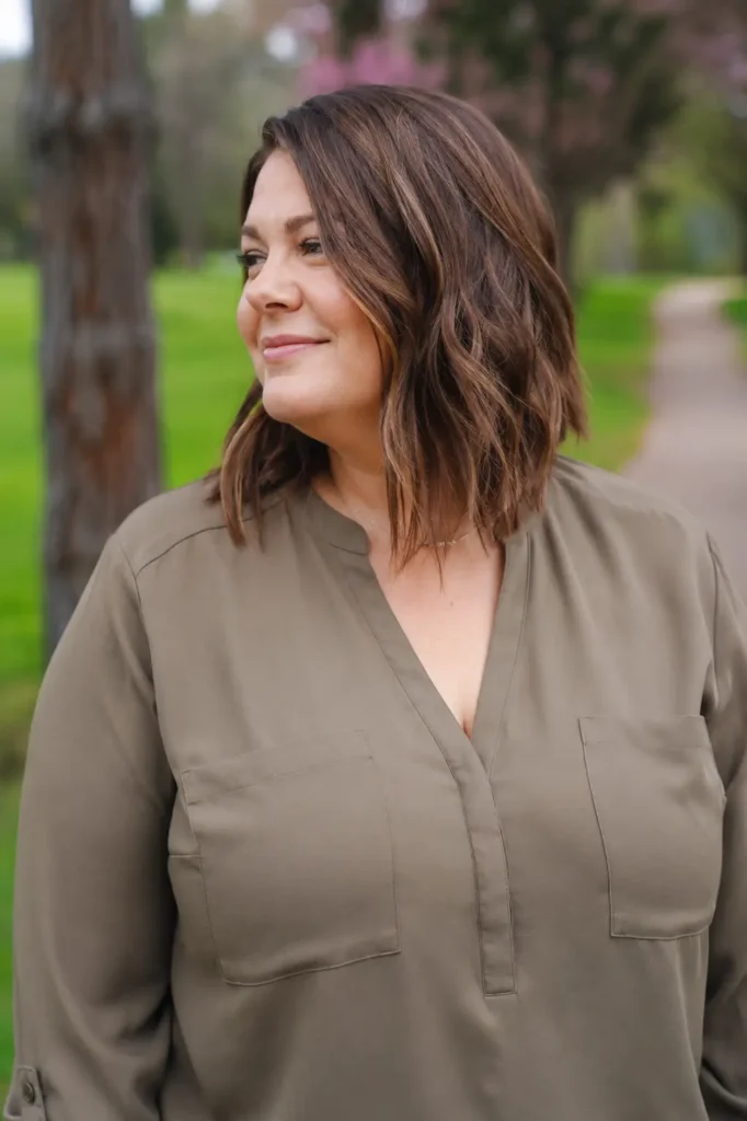 plus-size woman aged 30–50 with a textured long bob haircut in medium brown hair, photographed outdoors in a park during natural daylight