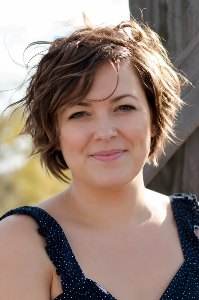woman with a round face wearing a tousled pixie bob haircut with textured layers and added crown height,