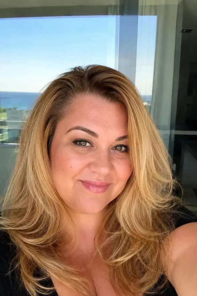 plus-size woman aged 30–45 with a medium-length voluminous blowout hairstyle in golden blonde, featuring glossy, healthy hair with luxurious body and shine