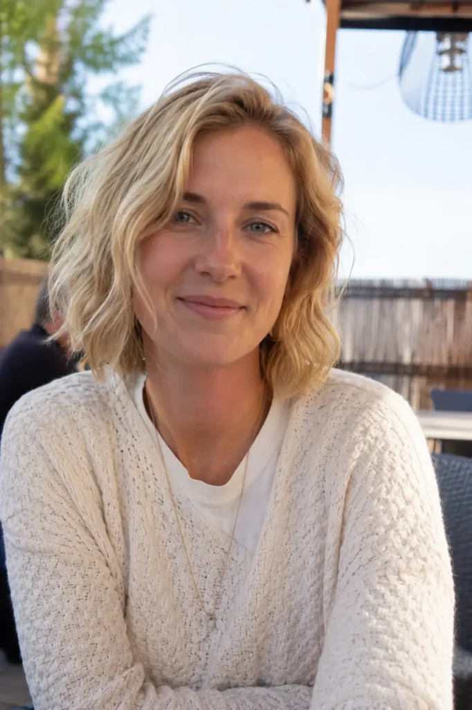 woman aged 25–40 with a wavy bob haircut and light blonde beachy waves, photographed in bright natural daylight. The close-up DSLR portrait highlights the textured, chin-length hairstyle with soft, tousled waves and natural volume.