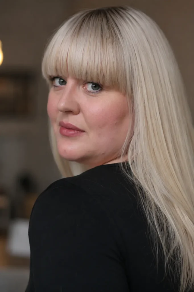 Plus-size English woman with blunt-cut bangs and long, straight platinum blonde hair, photographed in soft natural light